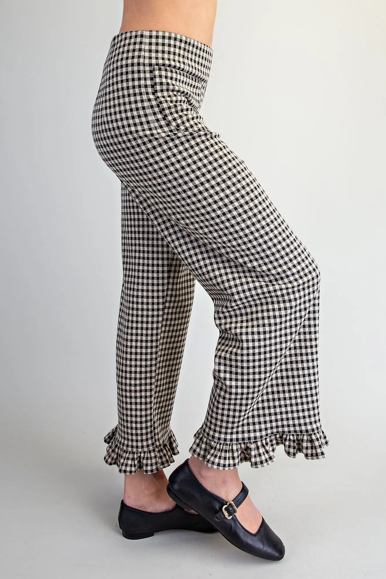 Black and white gingham wide-leg pants with ruffled hems, shown on a model from the waist down wearing black Mary Jane flats against a light gray background.