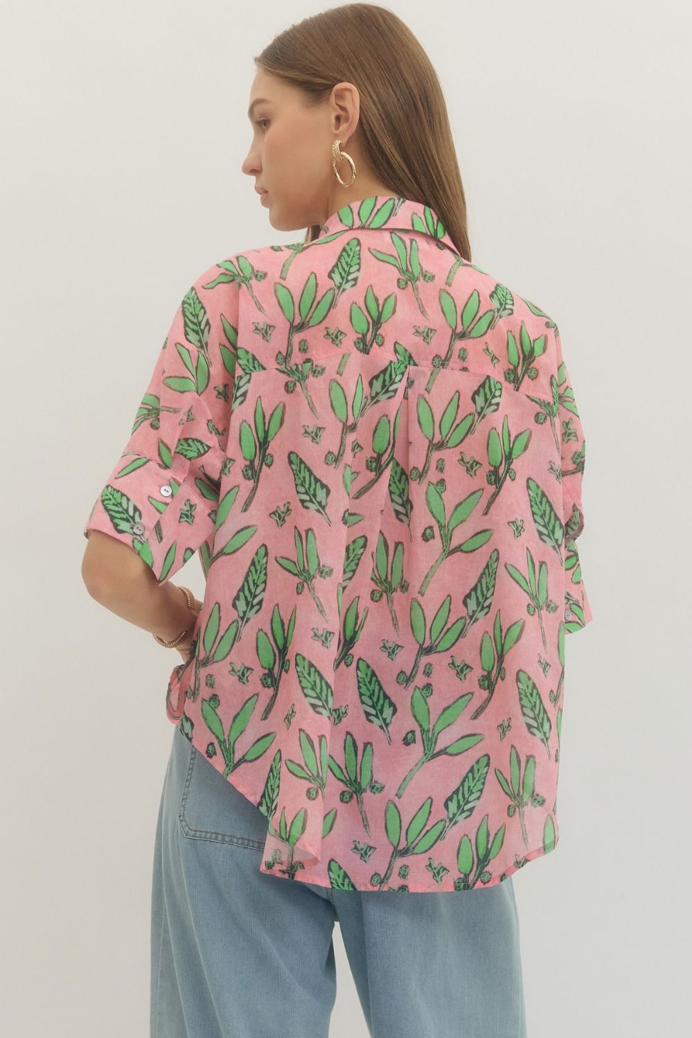 Person wearing a pink shirt with green leaf pattern and blue jeans on a light gray background