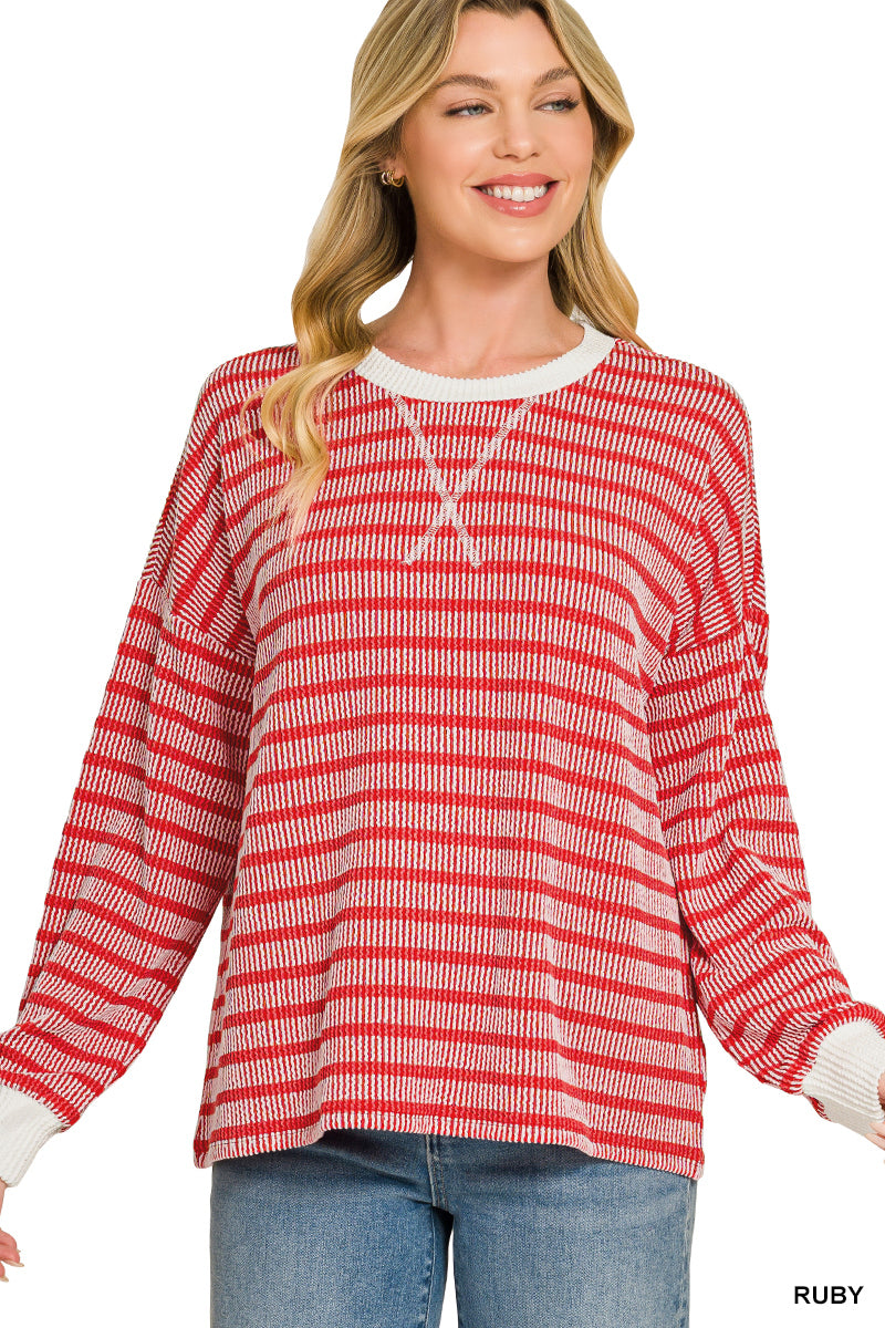 A woman wearing a red and white horizontally striped knit long-sleeve sweater with a white crew neck and cuffs, paired with blue jeans, against a plain white background.