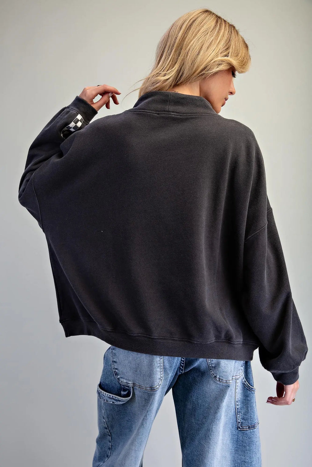 A person shown from the back wearing an oversized black sweatshirt and light blue jeans against a plain light gray studio background.