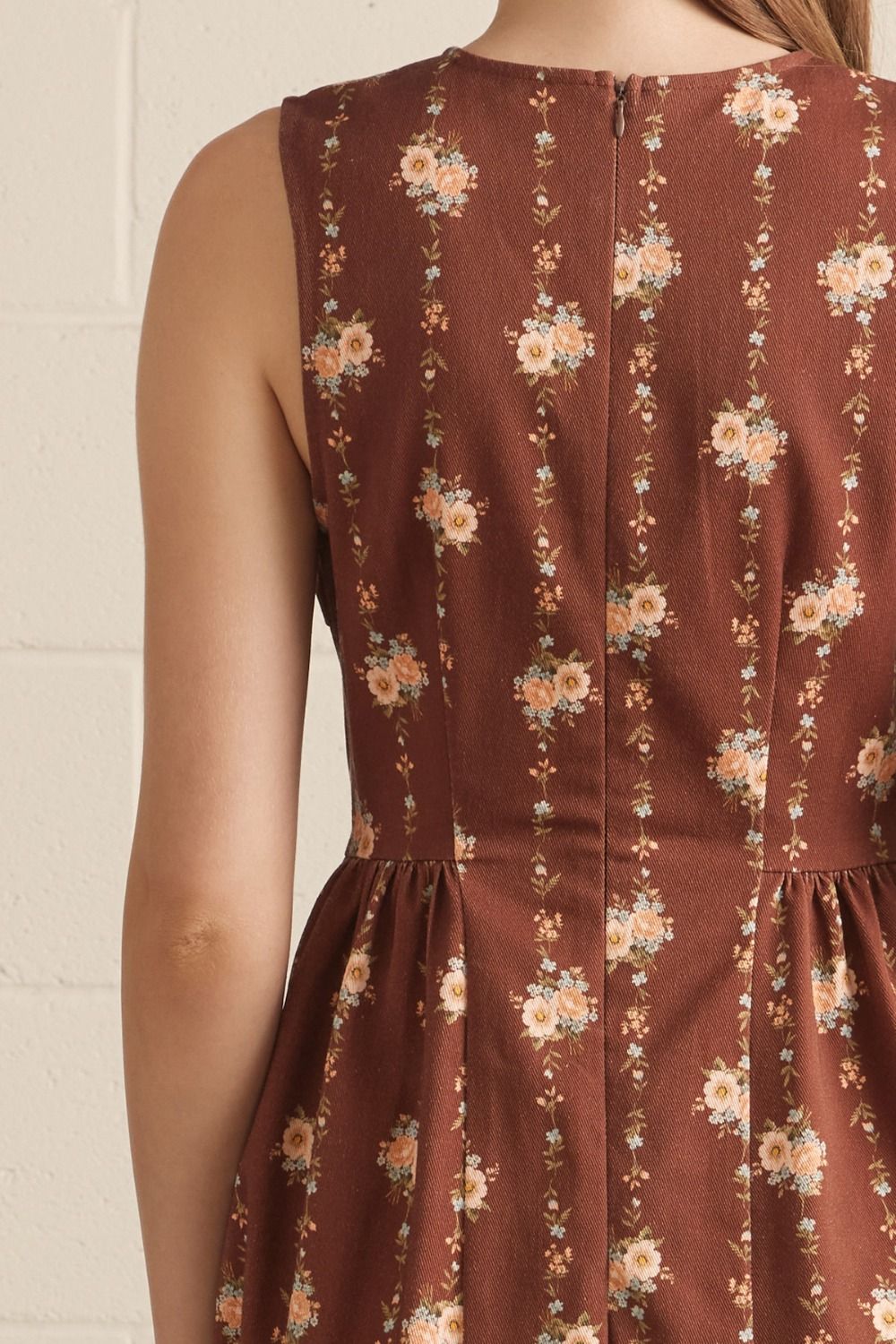 Brown floral dress worn by a person against a white brick wall.
