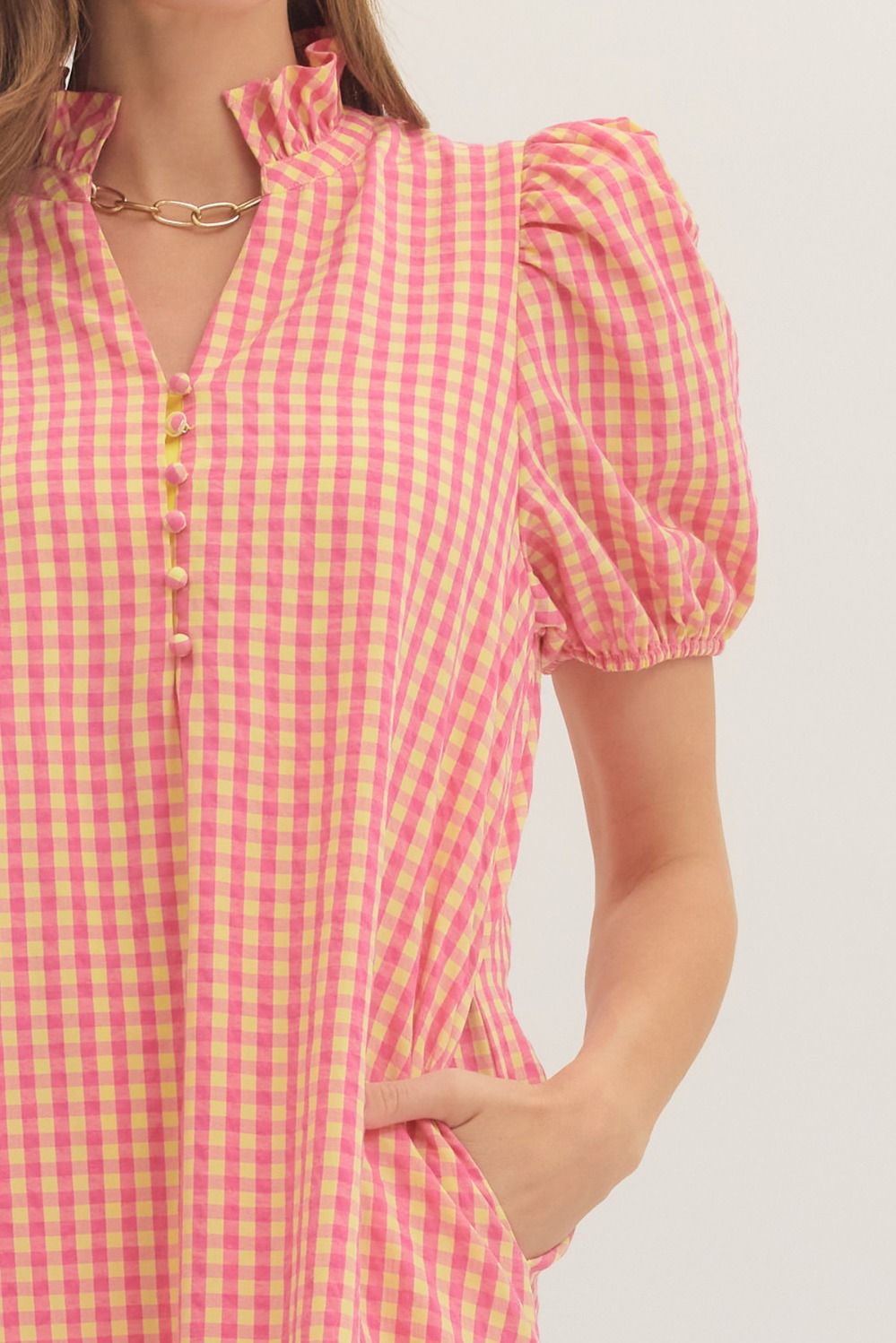 Person wearing a pink and yellow checkered dress with short sleeves on a white background