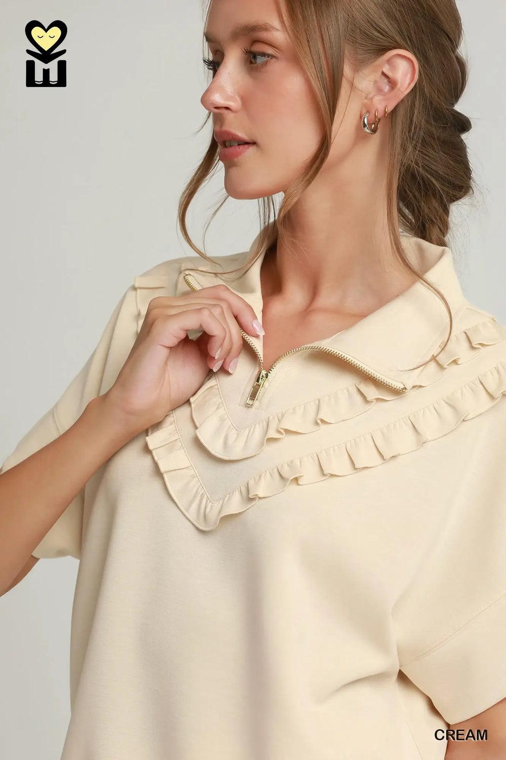 Woman wearing a cream blouse with ruffled collar against a plain background