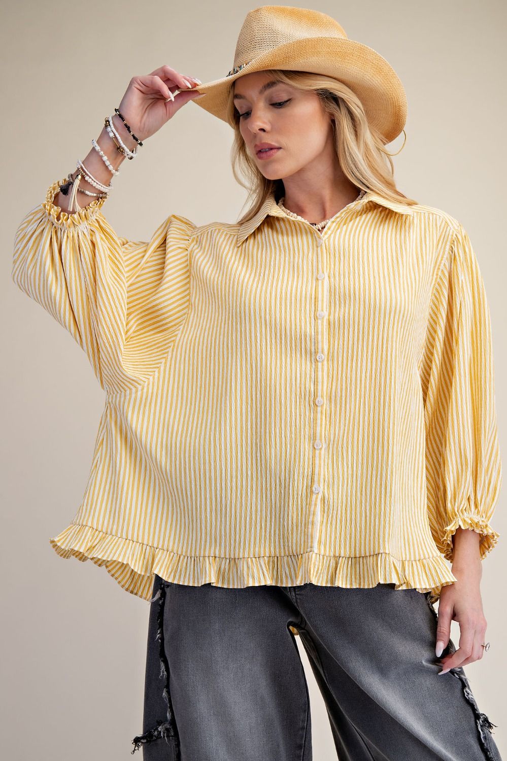 Woman wearing a yellow striped blouse and beige hat against a neutral background
