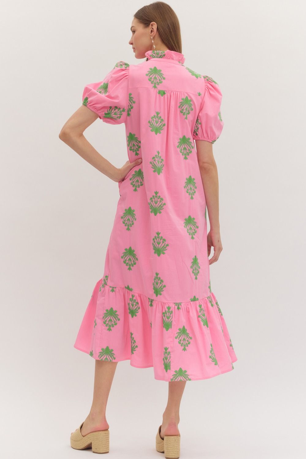Woman wearing a pink dress with green floral patterns on a white background