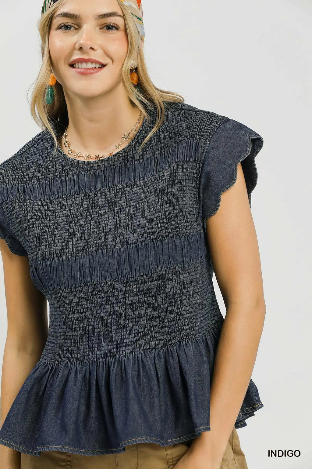Woman wearing a dark blue smocked top with ruffled details on a white background