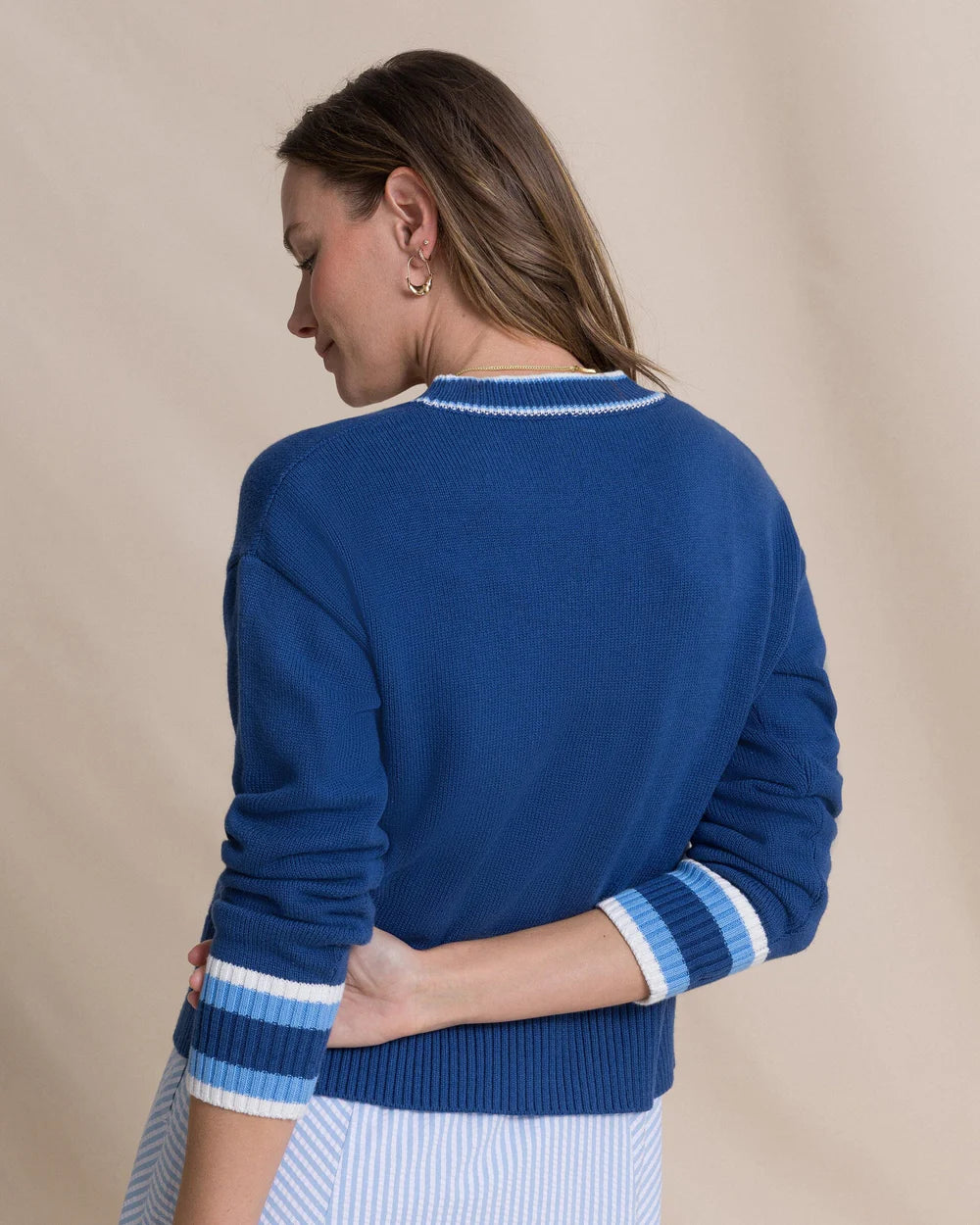 Woman wearing a blue sweater with white trim on a beige background