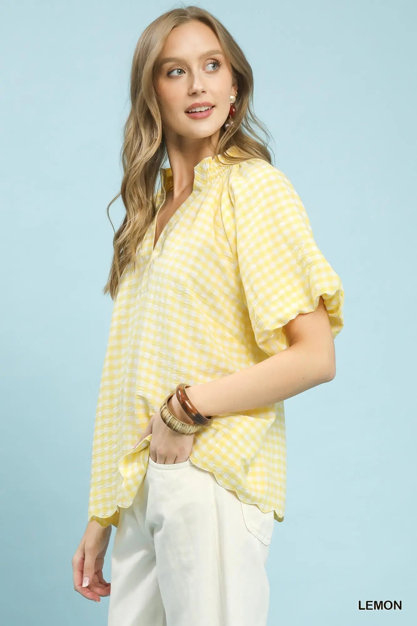 Woman wearing a yellow patterned top and white pants against a light blue background