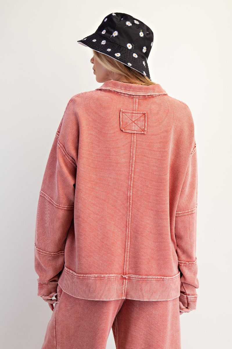 Person wearing a pink distressed jacket and pants with a black floral hat on a white background