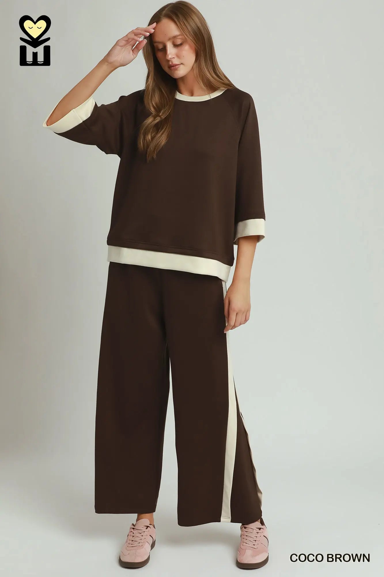 Woman wearing a brown outfit with white accents on a plain background