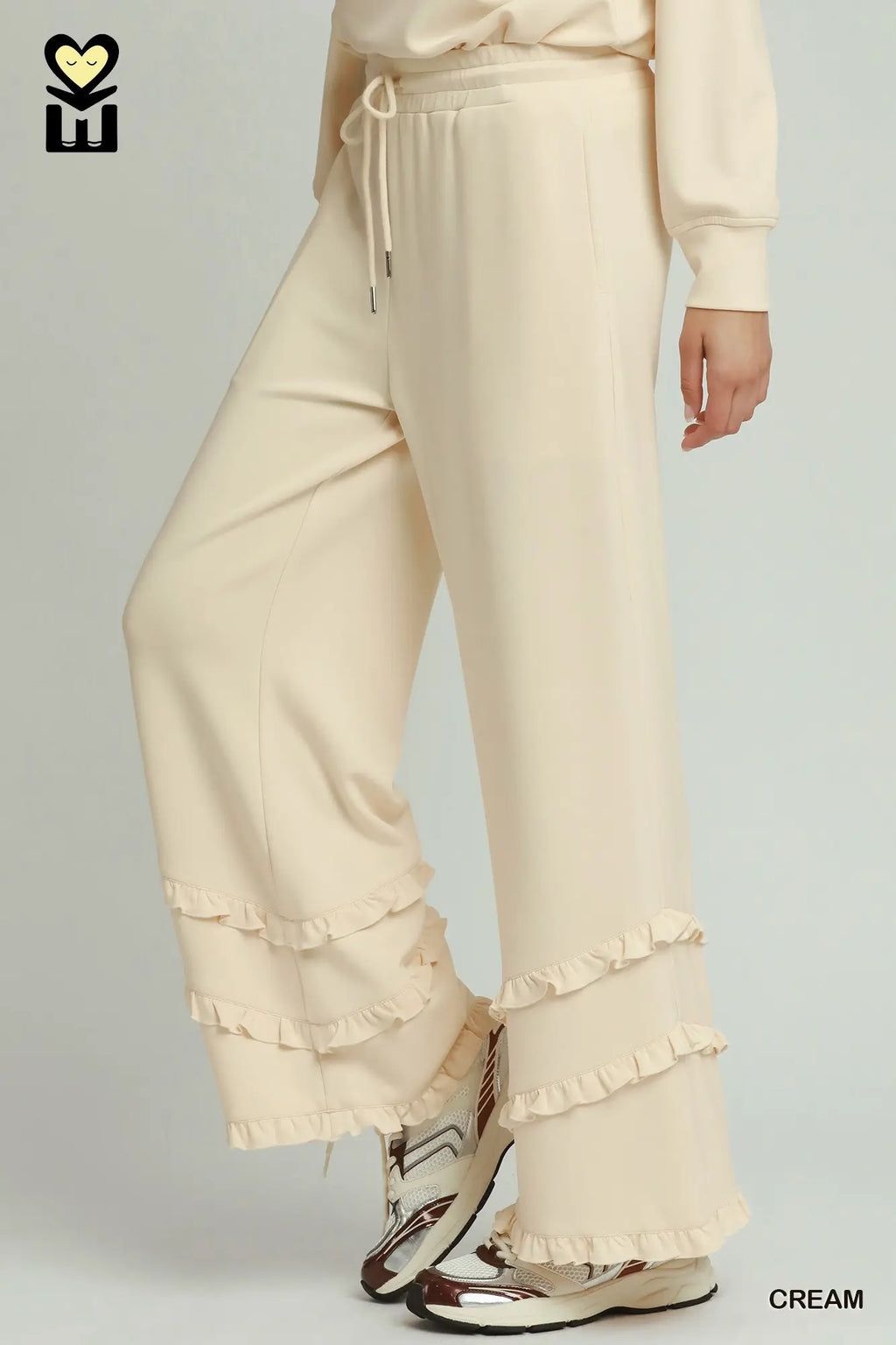 Beige pants with ruffled details worn by a person on a gray background