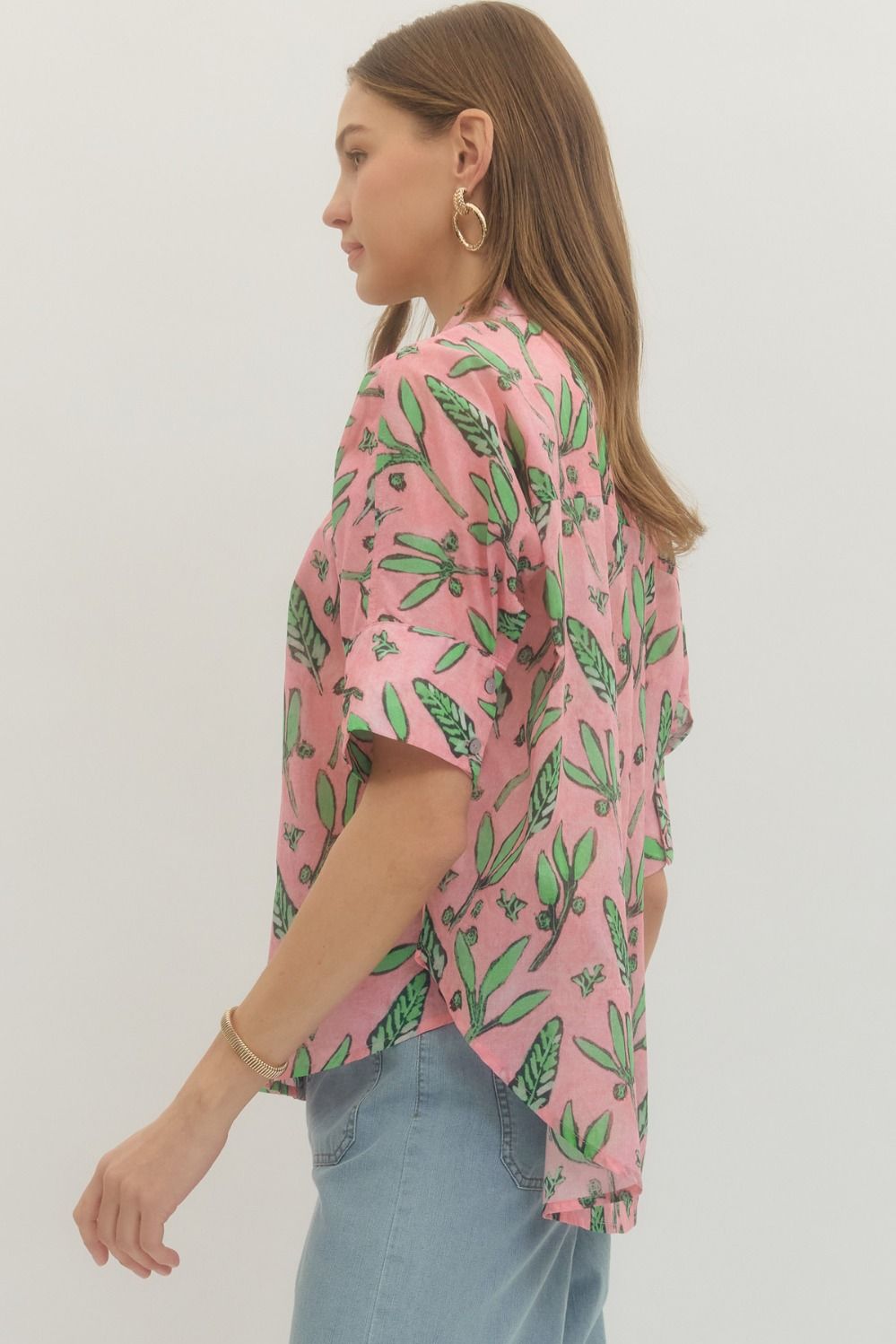 Woman wearing a pink shirt with green leaf pattern and light blue jeans on a white background