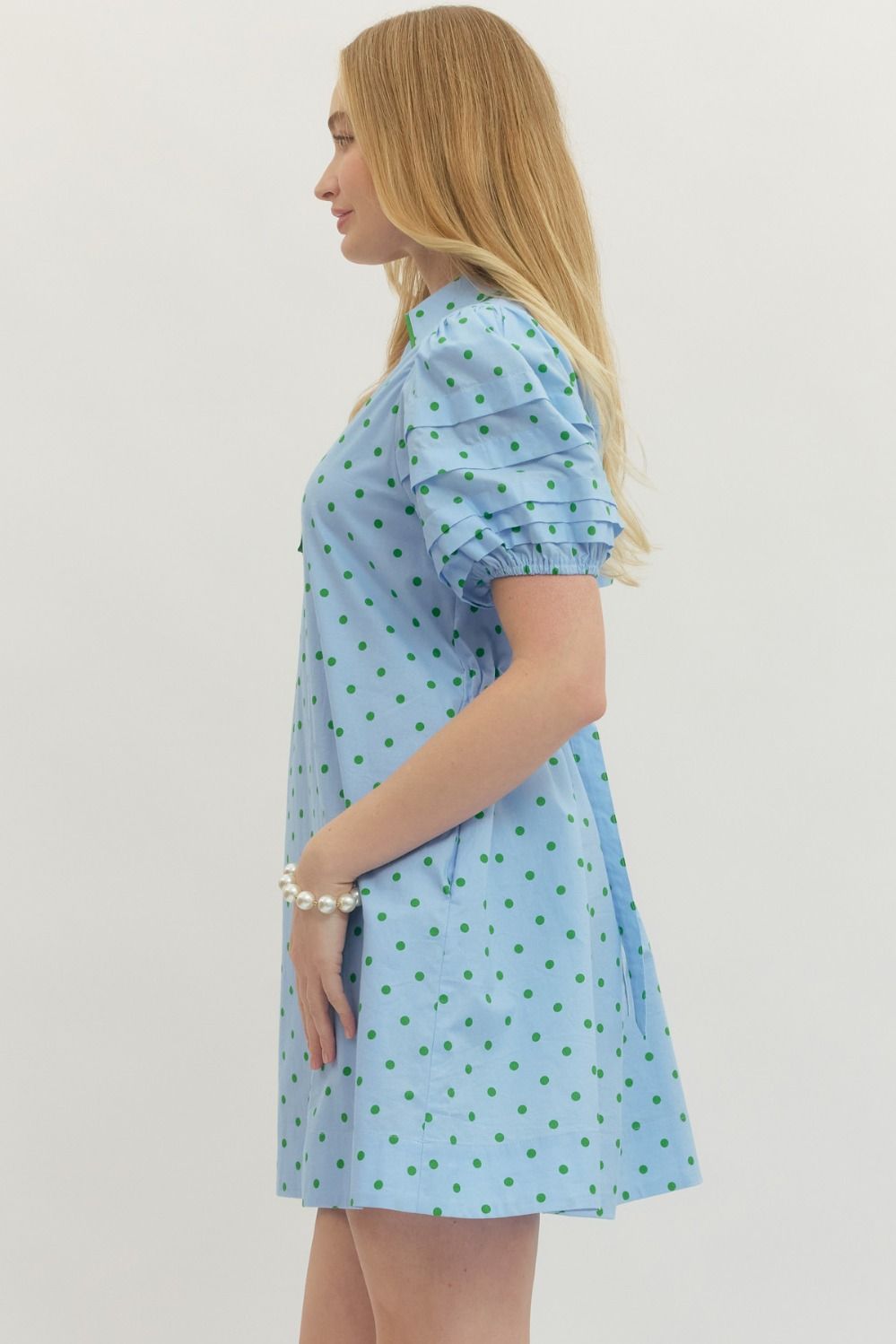 Woman wearing a light blue dress with green polka dots on a plain background