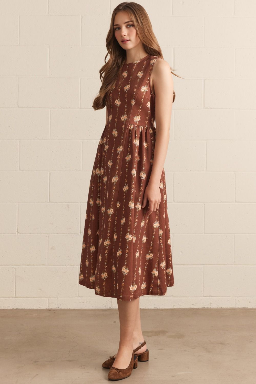 Woman wearing a brown floral dress against a white brick wall.