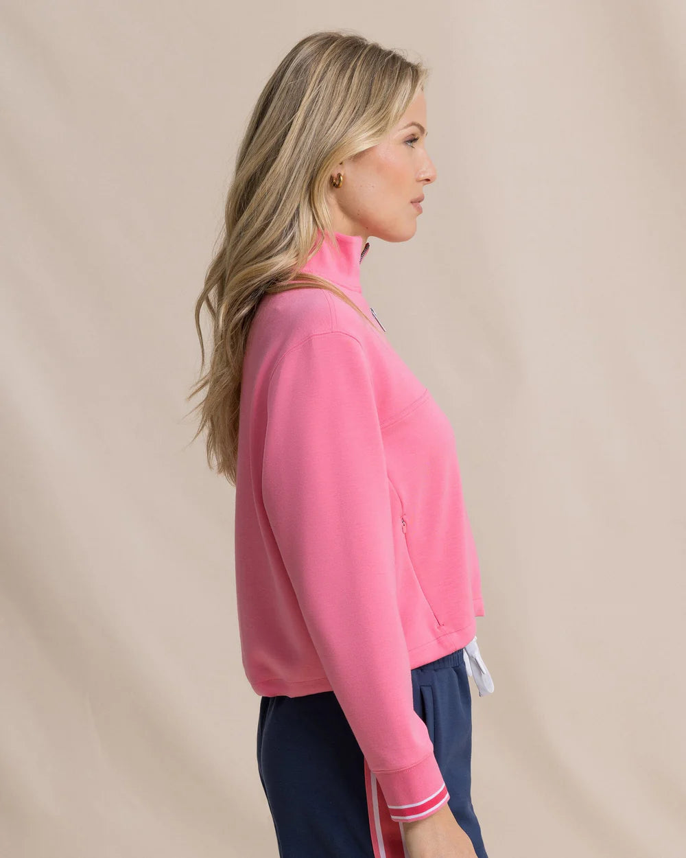 Woman wearing a pink jacket and navy pants against a beige background