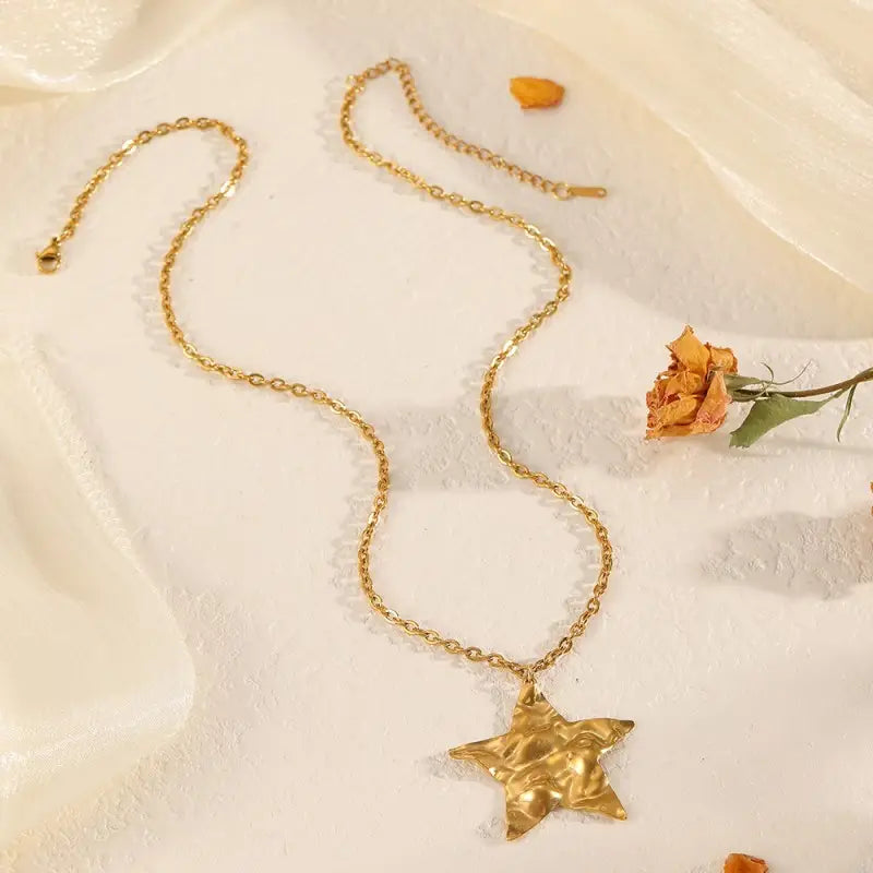 Gold star necklace on a soft fabric background with a dried flower.