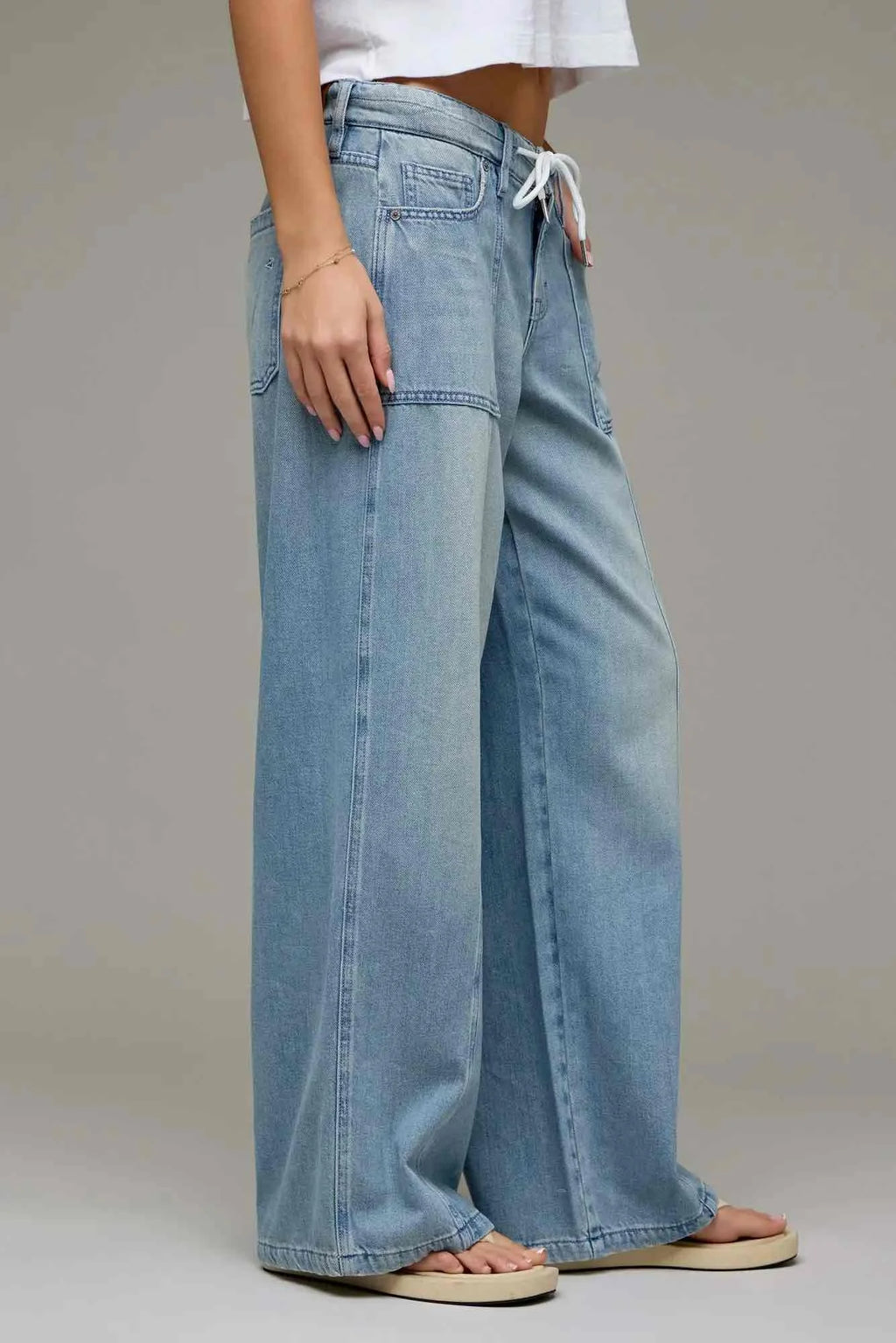 A person wearing light blue wide-leg denim jeans with a drawstring waist, shown from the waist down against a plain gray studio background.