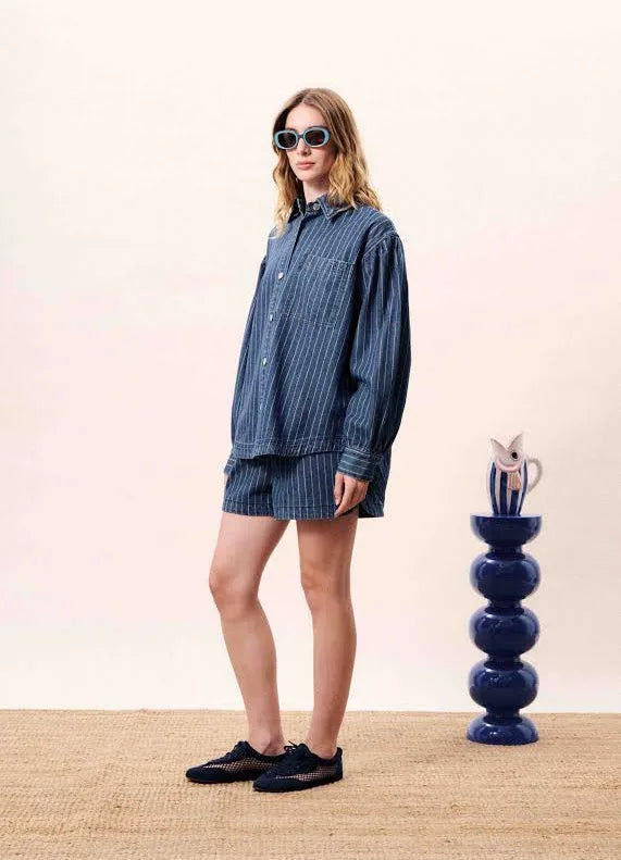 Woman wearing a blue striped outfit standing next to a decorative vase on a beige floor.
