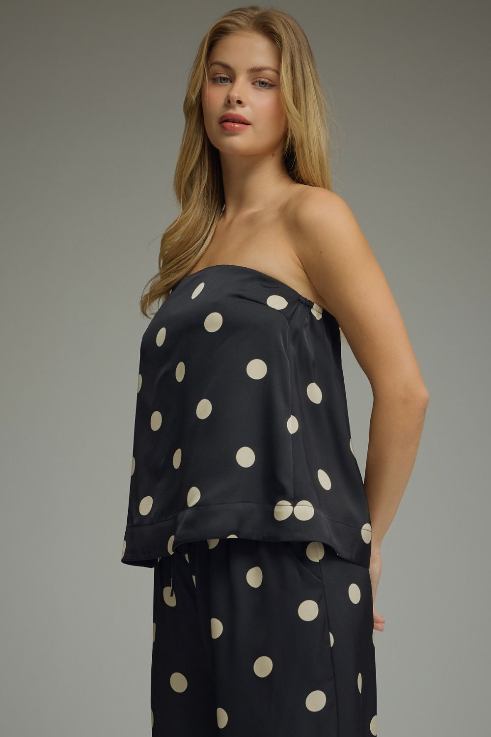 Woman wearing a black strapless top with white polka dots on a gray background