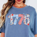 Blue t-shirt with '1776' design featuring stars, stripes, and checkered patterns.