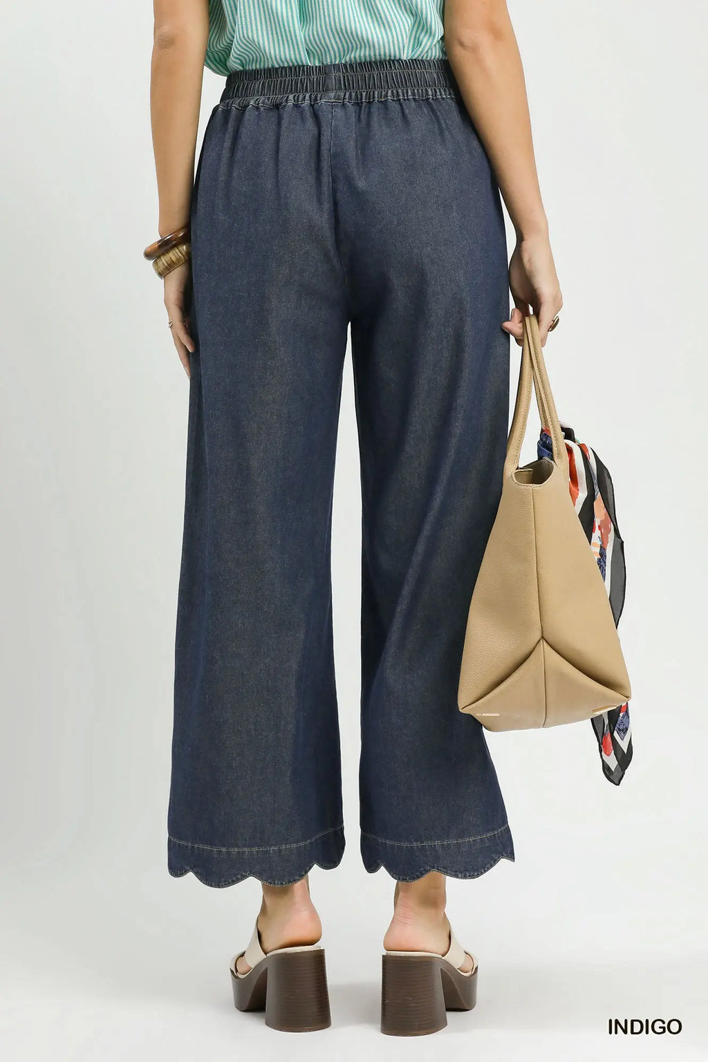 Person wearing blue jeans and holding a beige handbag on a white background