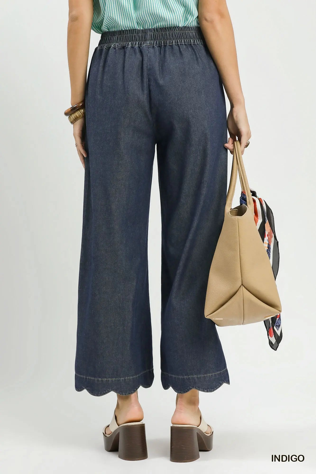 Person wearing blue jeans and holding a beige handbag on a white background