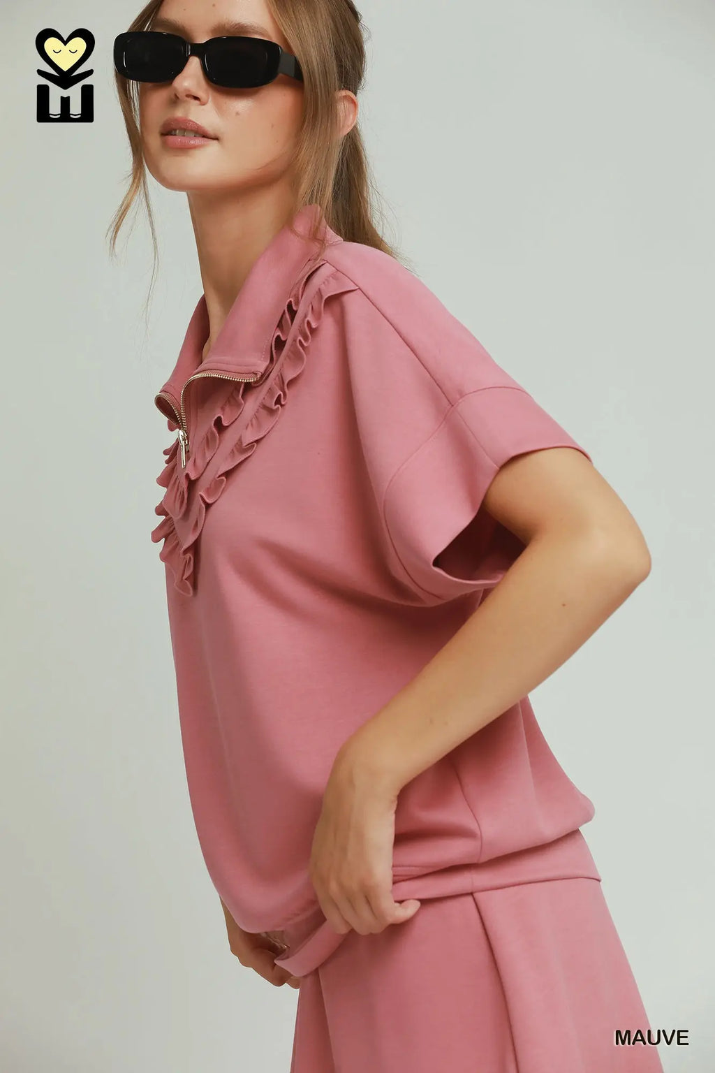 Woman wearing a mauve outfit with ruffled details on a plain background