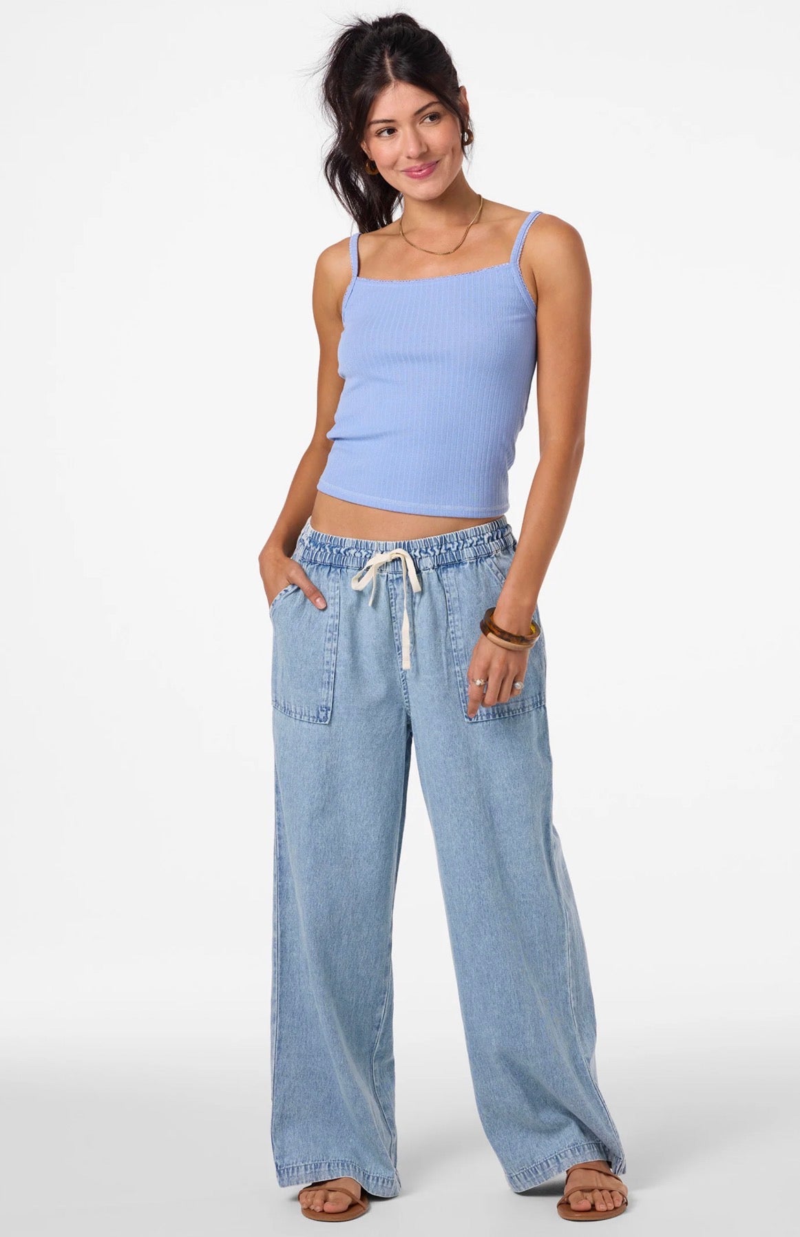 Woman wearing a light blue tank top and denim pants on a white background