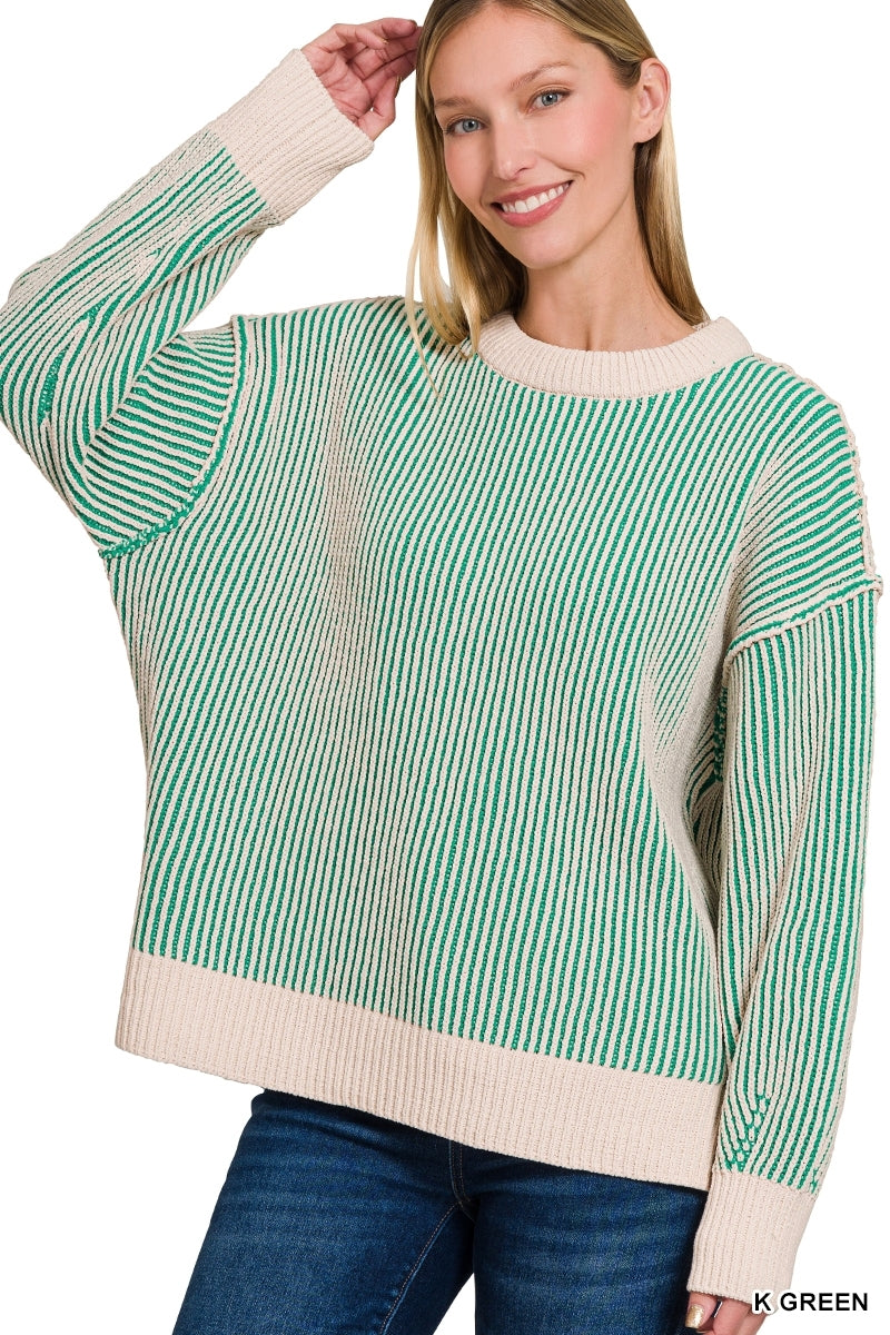 A woman wearing a green and cream striped knit sweater with blue jeans, shown against a plain white background.