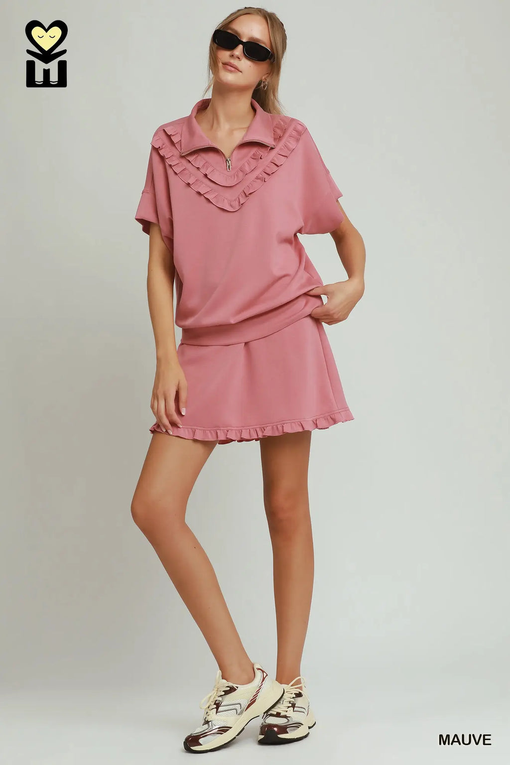 Woman wearing a mauve outfit with ruffled details on a plain background