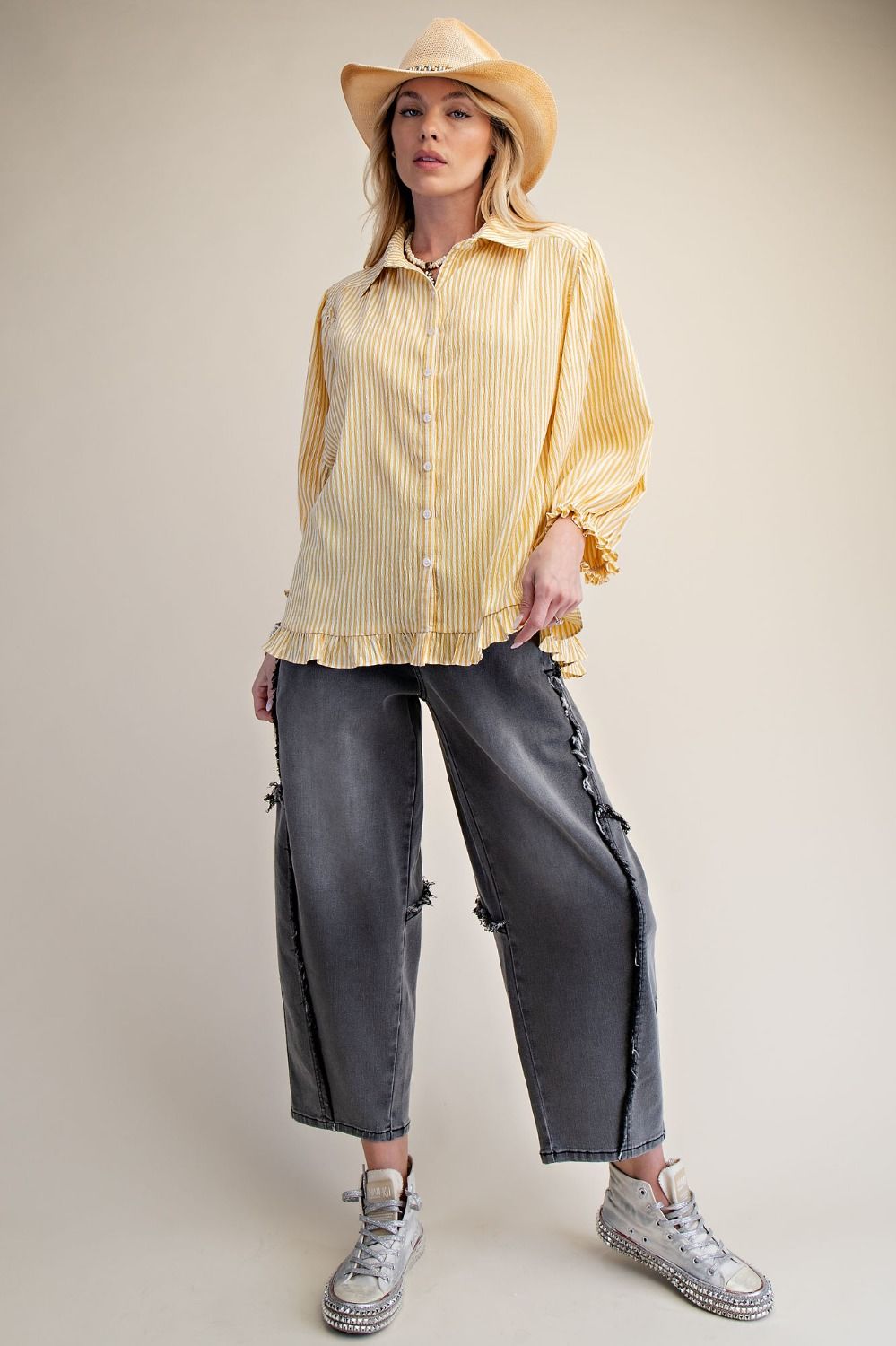 Person wearing a yellow striped shirt, gray pants, and a beige cowboy hat on a plain background