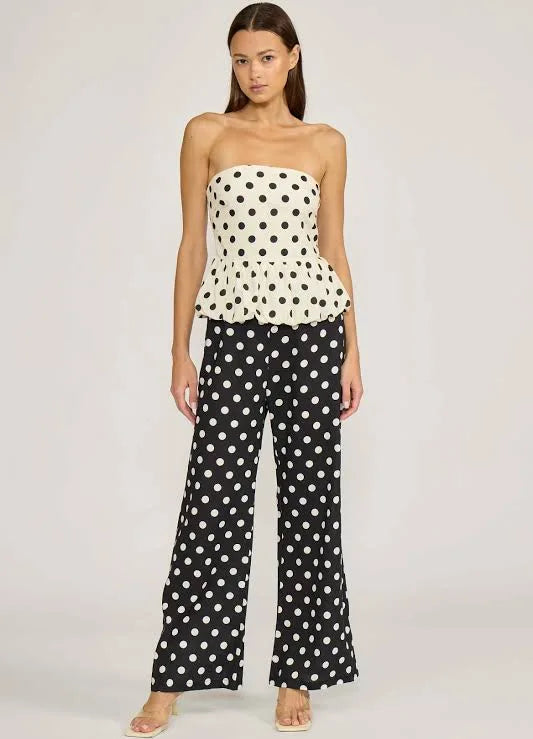 Woman wearing a polka dot strapless top and wide-leg pants on a plain background
