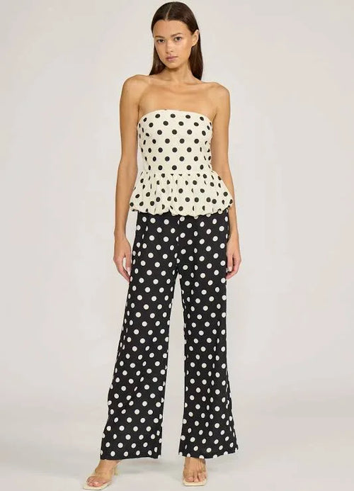 Woman wearing a polka dot strapless top and wide-leg pants on a plain background