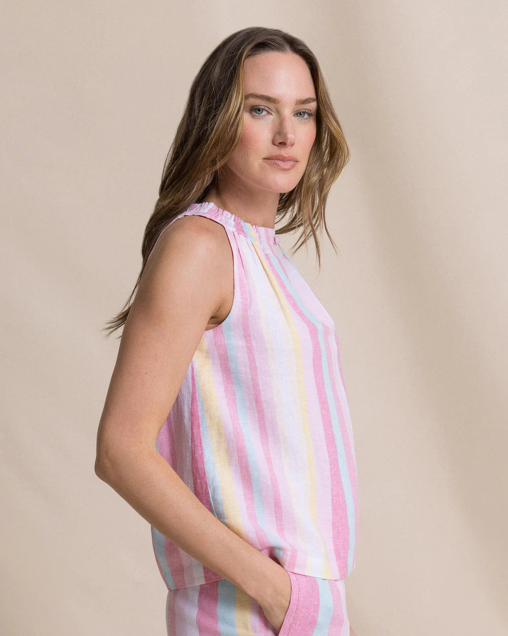 Woman wearing a sleeveless, multicolored striped top against a beige background