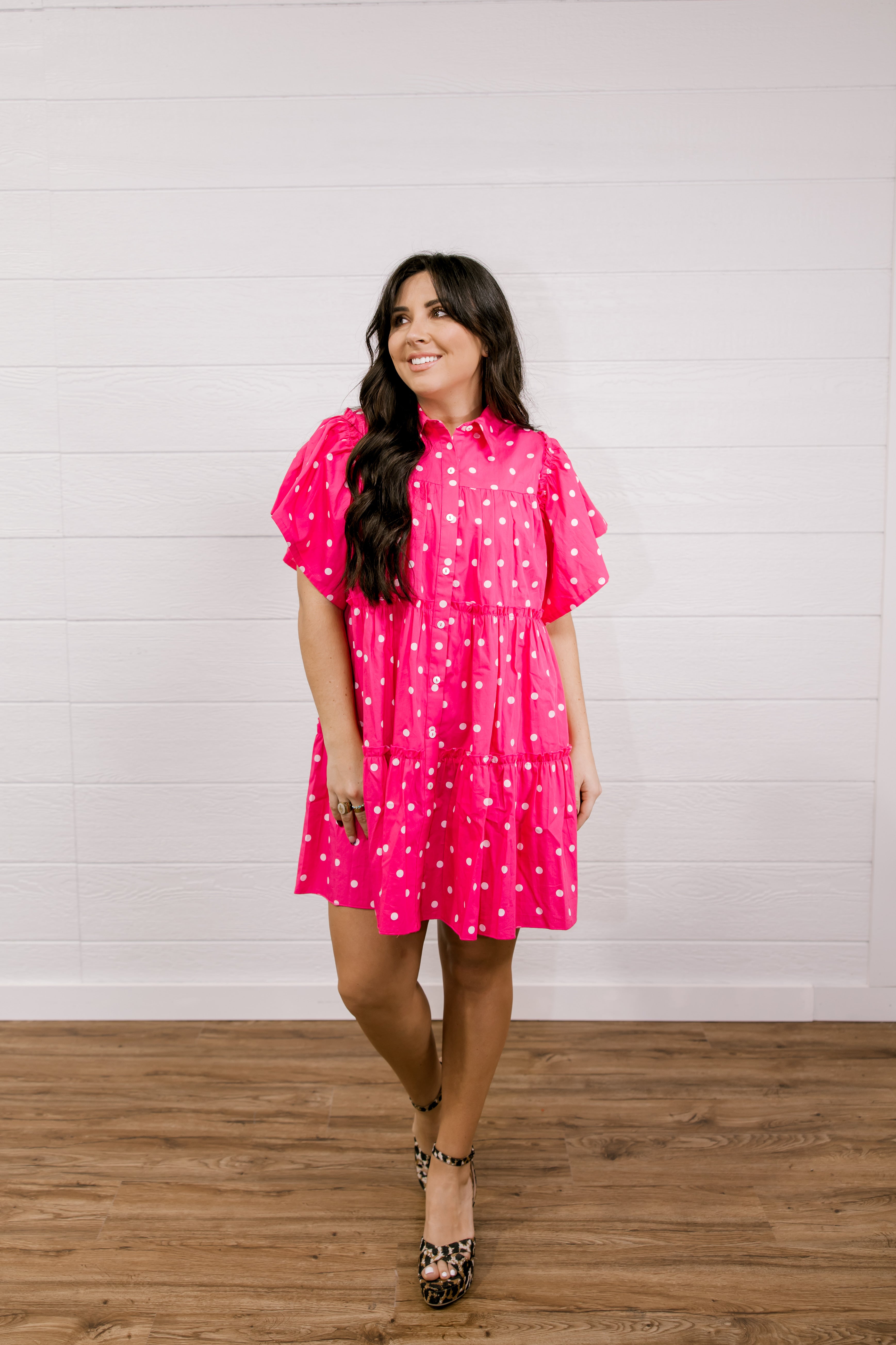 Woman wearing a pink polka dot dress standing against a white wall.