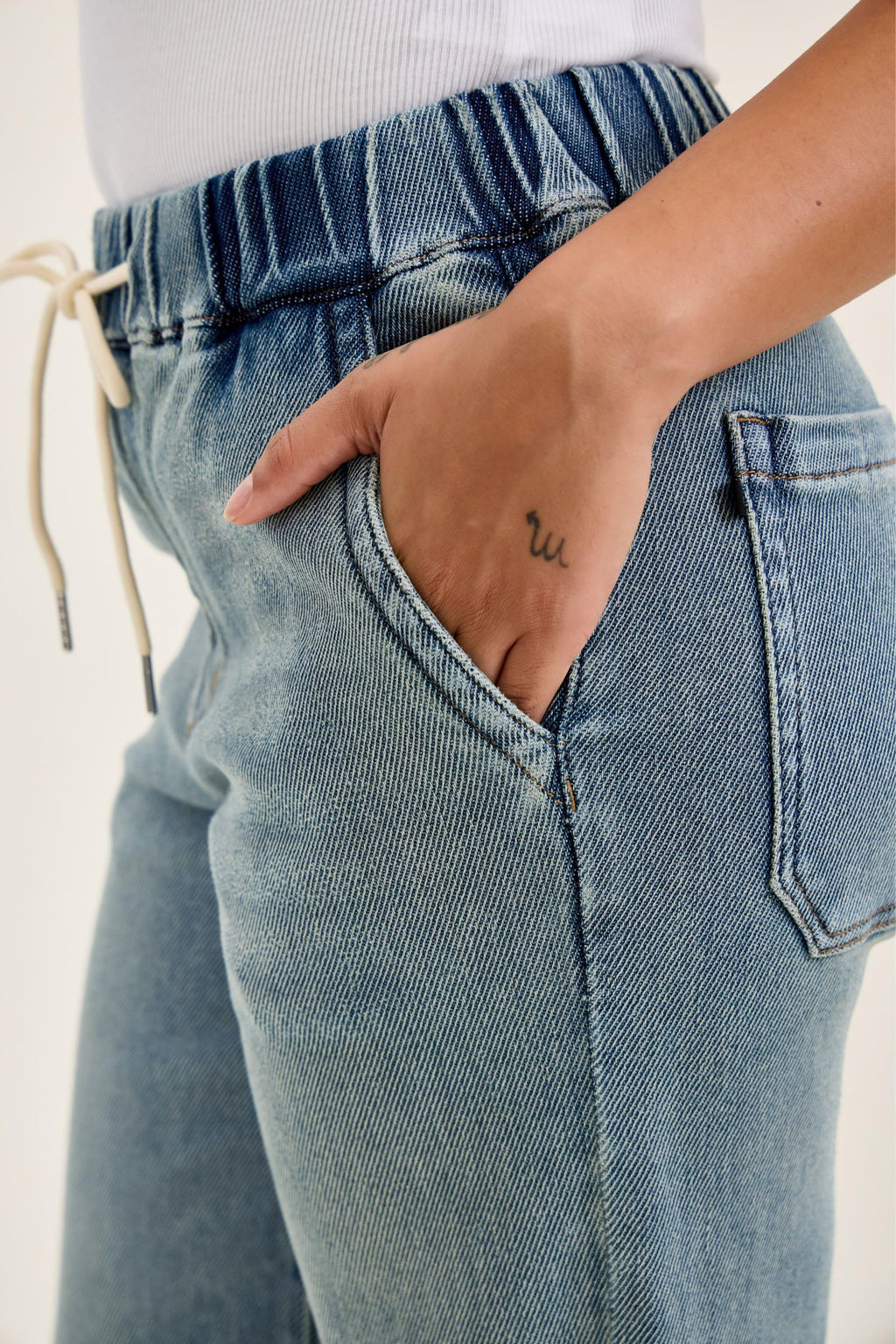 Close-up of blue jeans with a hand in the pocket on a plain background