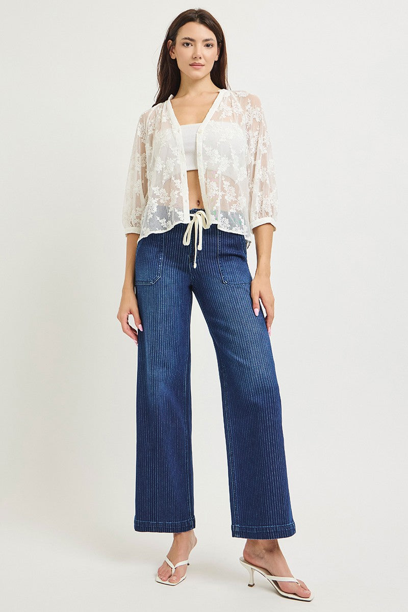 Woman wearing a white lace top and blue jeans on a white background