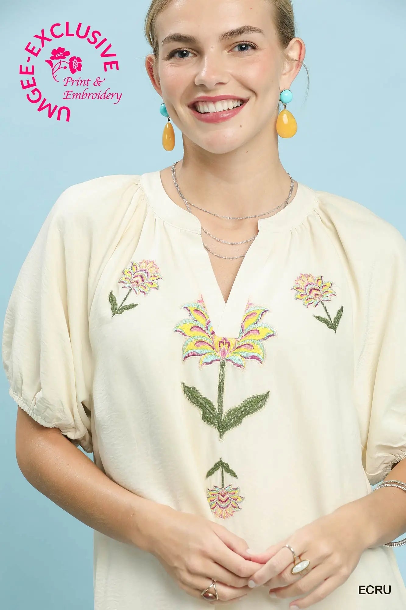 Woman wearing a cream blouse with floral embroidery against a light blue background