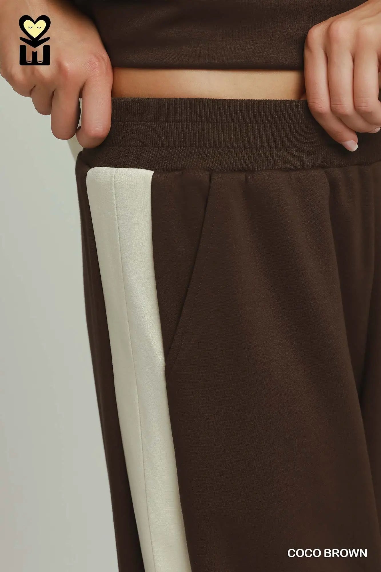 Brown pants with a white stripe being adjusted, on a plain background.