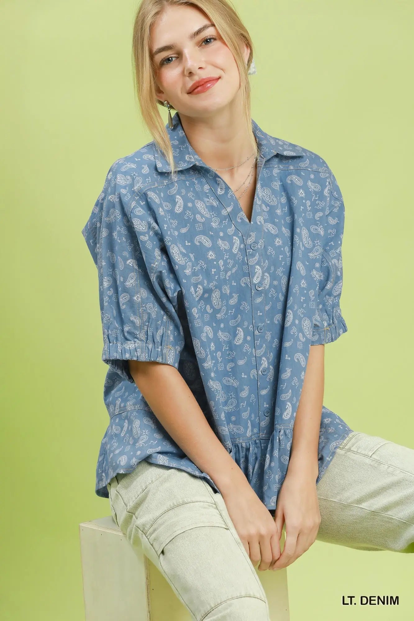 Woman wearing a blue patterned shirt sitting on a chair against a green background