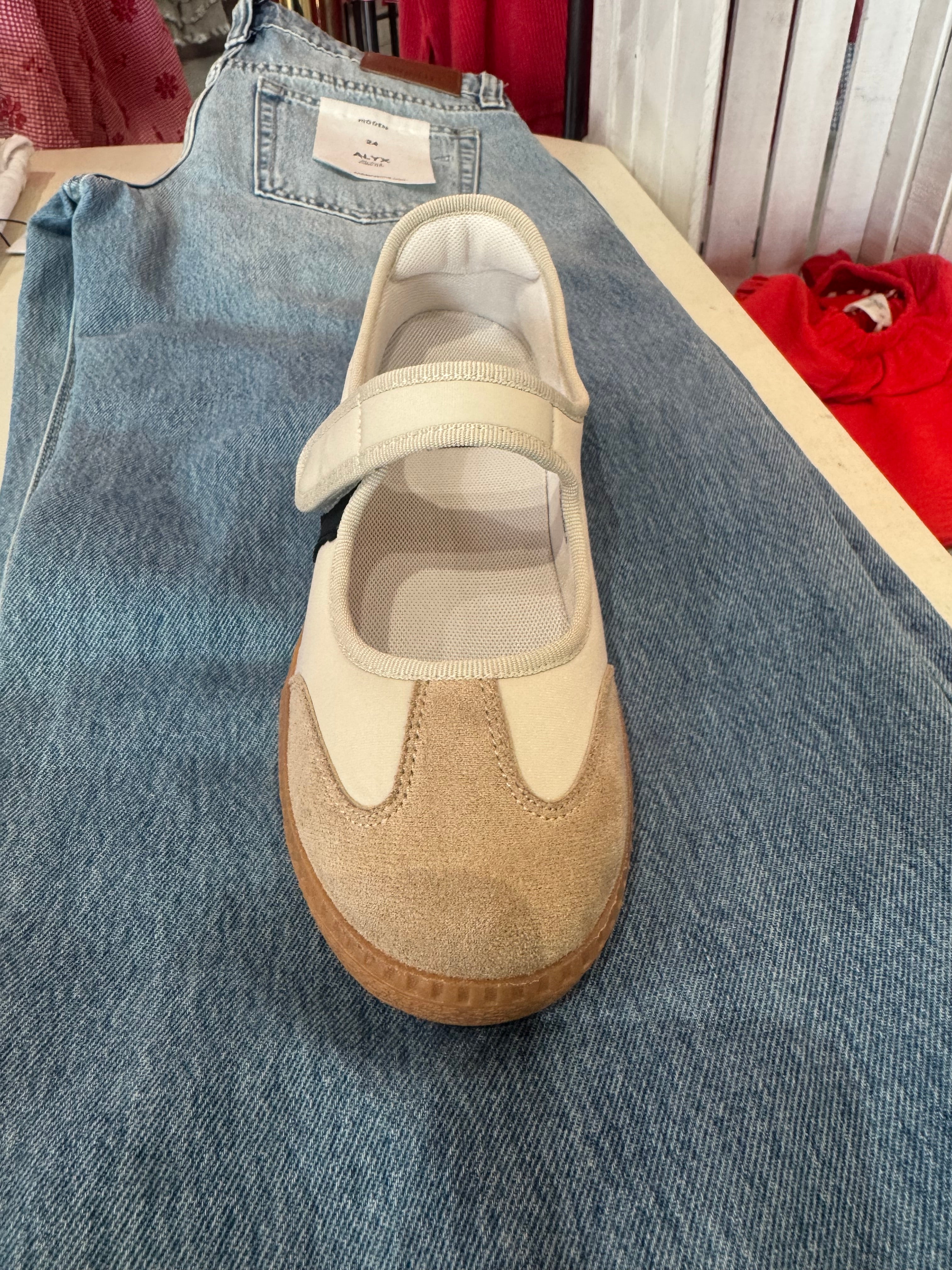 A beige and cream Mary Jane shoe with a brown gum sole, displayed on top of a pair of folded blue jeans.