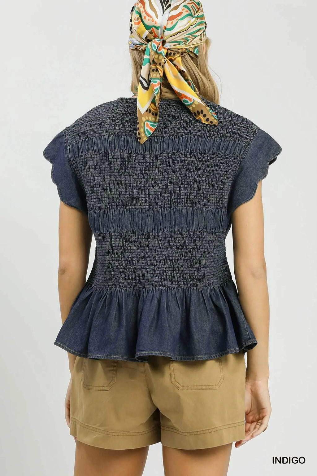 Person wearing a denim peplum top and beige shorts with a patterned headscarf on a white background