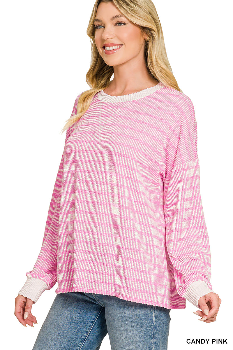 A woman wearing a pink and white horizontally striped long-sleeve knit top with solid white ribbed cuffs and collar, paired with blue jeans against a white background.
