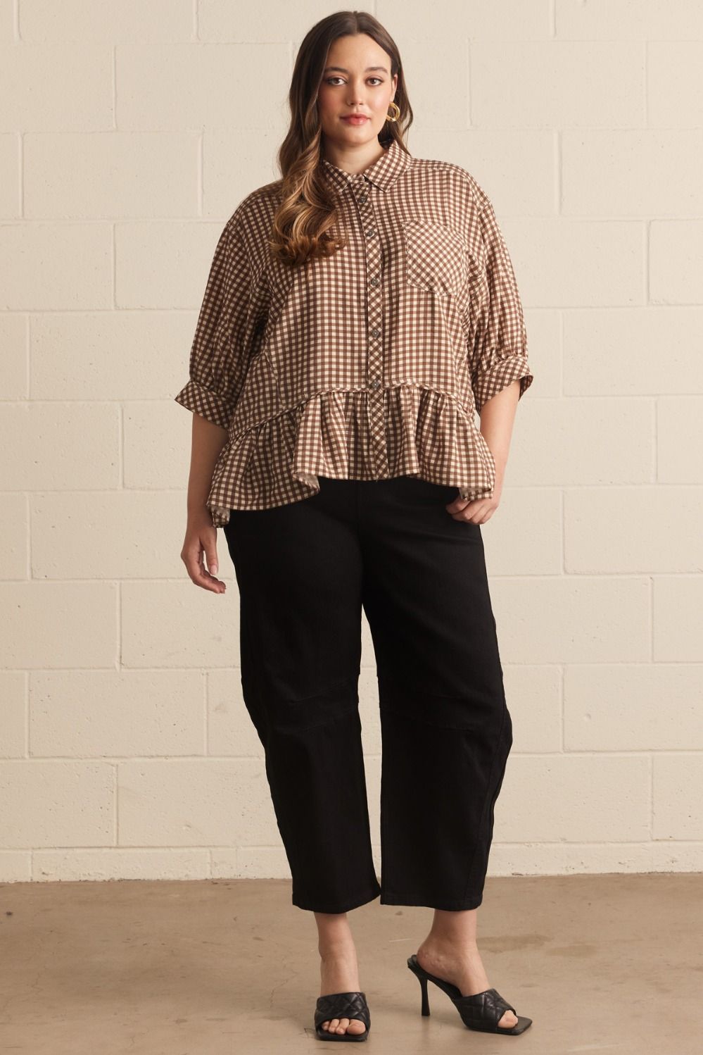 Woman wearing a checkered blouse and black pants against a beige wall.