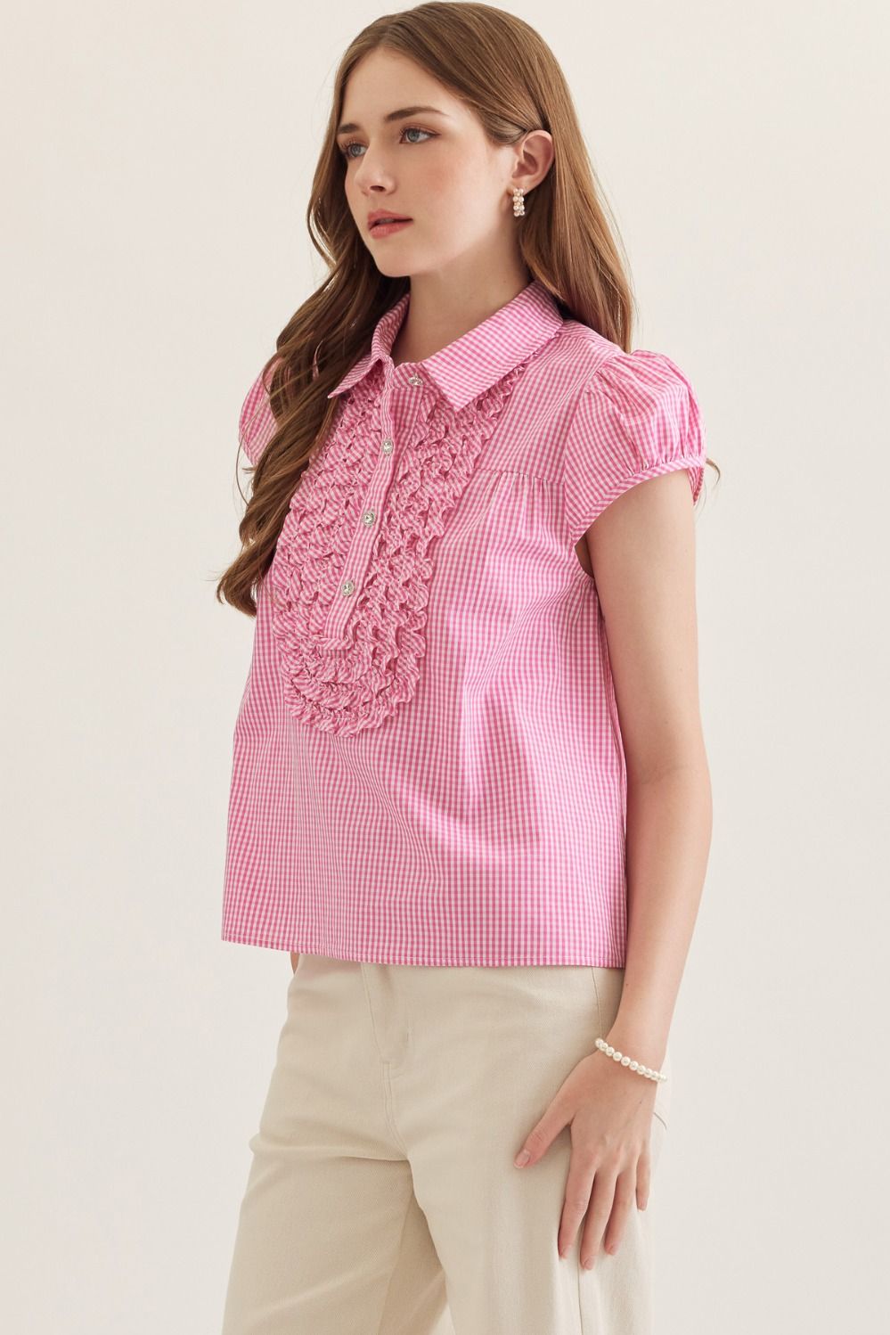 Woman wearing a pink checkered blouse with ruffled details on a light background