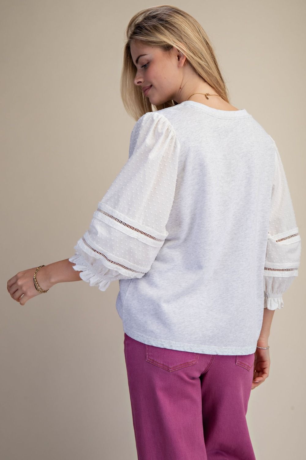 Woman wearing a white blouse with lace sleeves and pink pants on a beige background