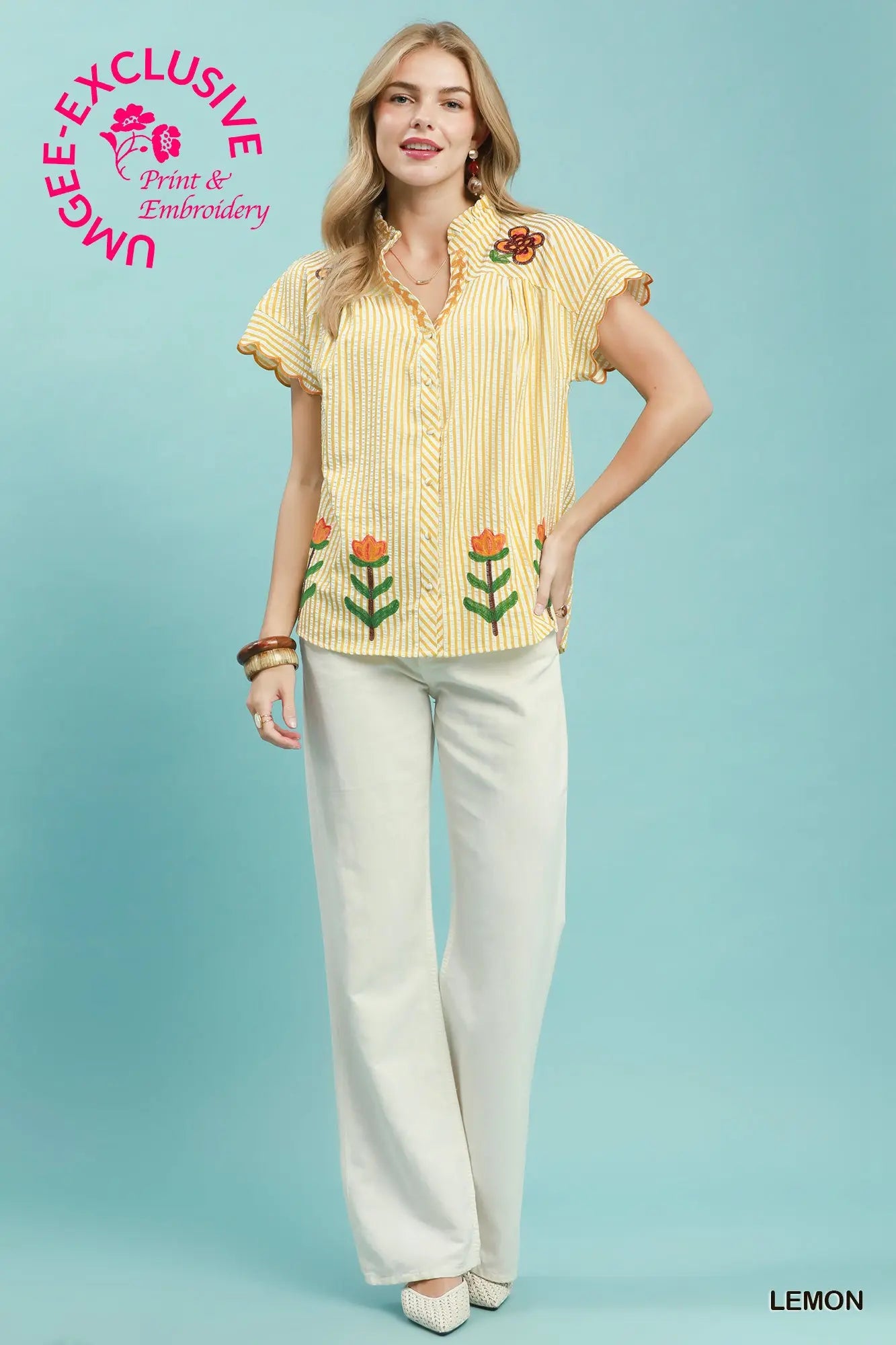 Woman wearing a yellow floral blouse and white pants on a light blue background with 'Muggee Exclusive' branding.