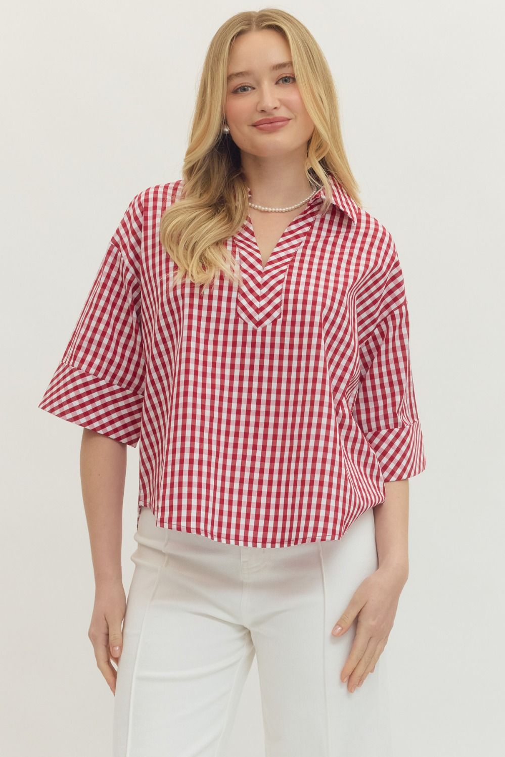 Woman wearing a red and white checkered shirt with white pants on a plain background