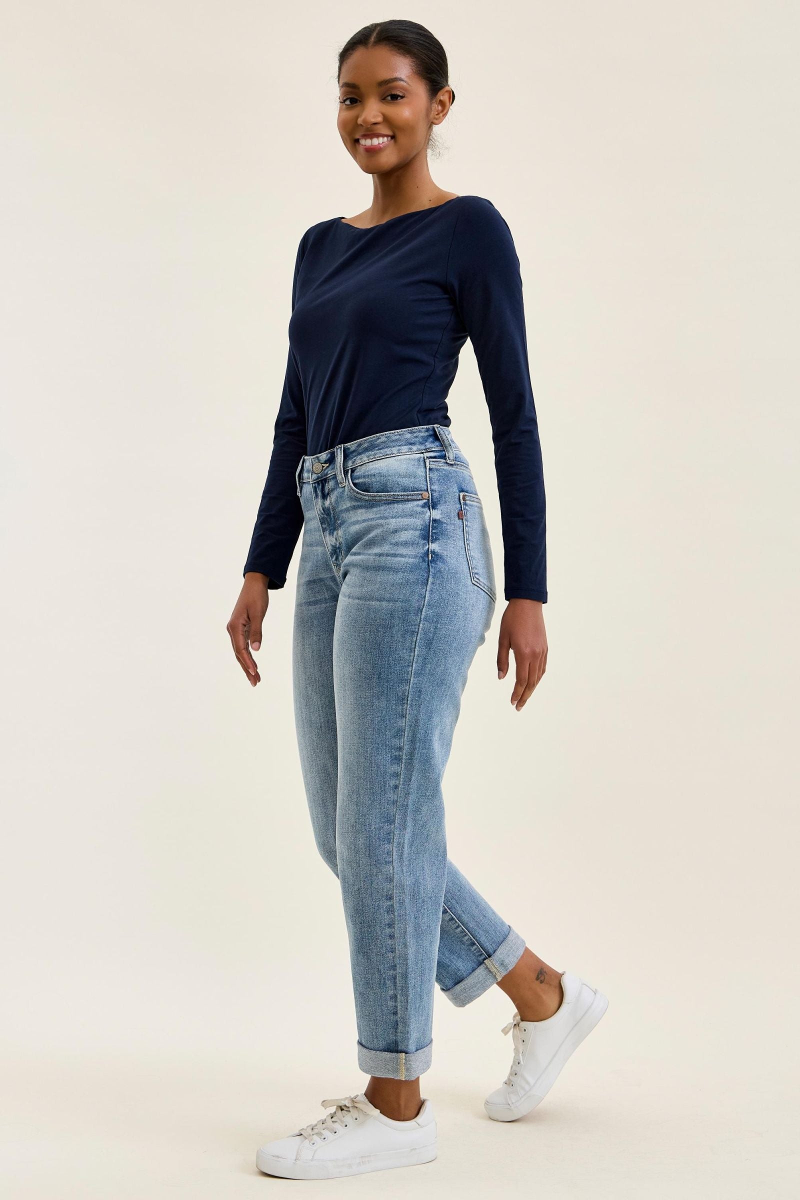 Woman wearing a navy long-sleeve top and light blue jeans on a beige background