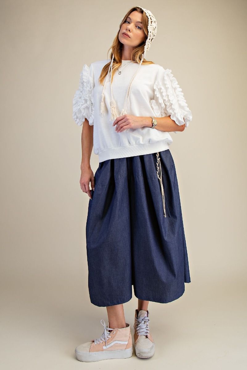 Woman wearing a white blouse with ruffled sleeves and navy blue pants on a beige background